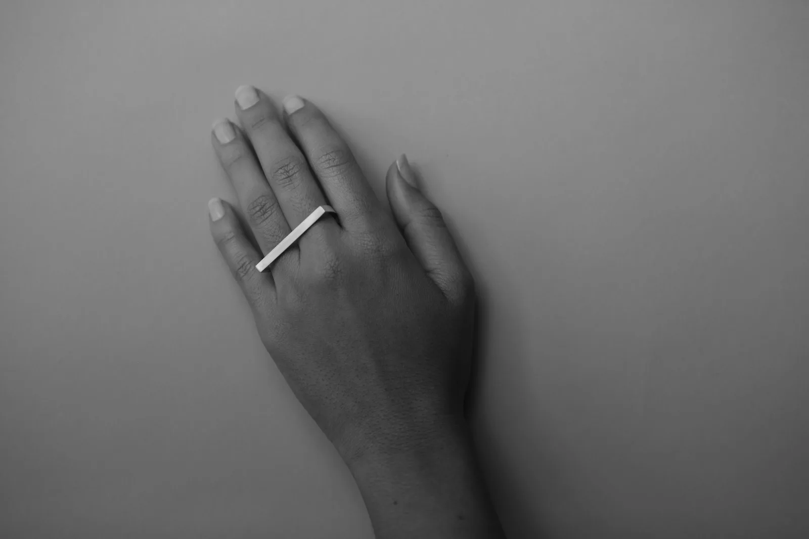 Hand wearing a silver bar ring on a neutral background