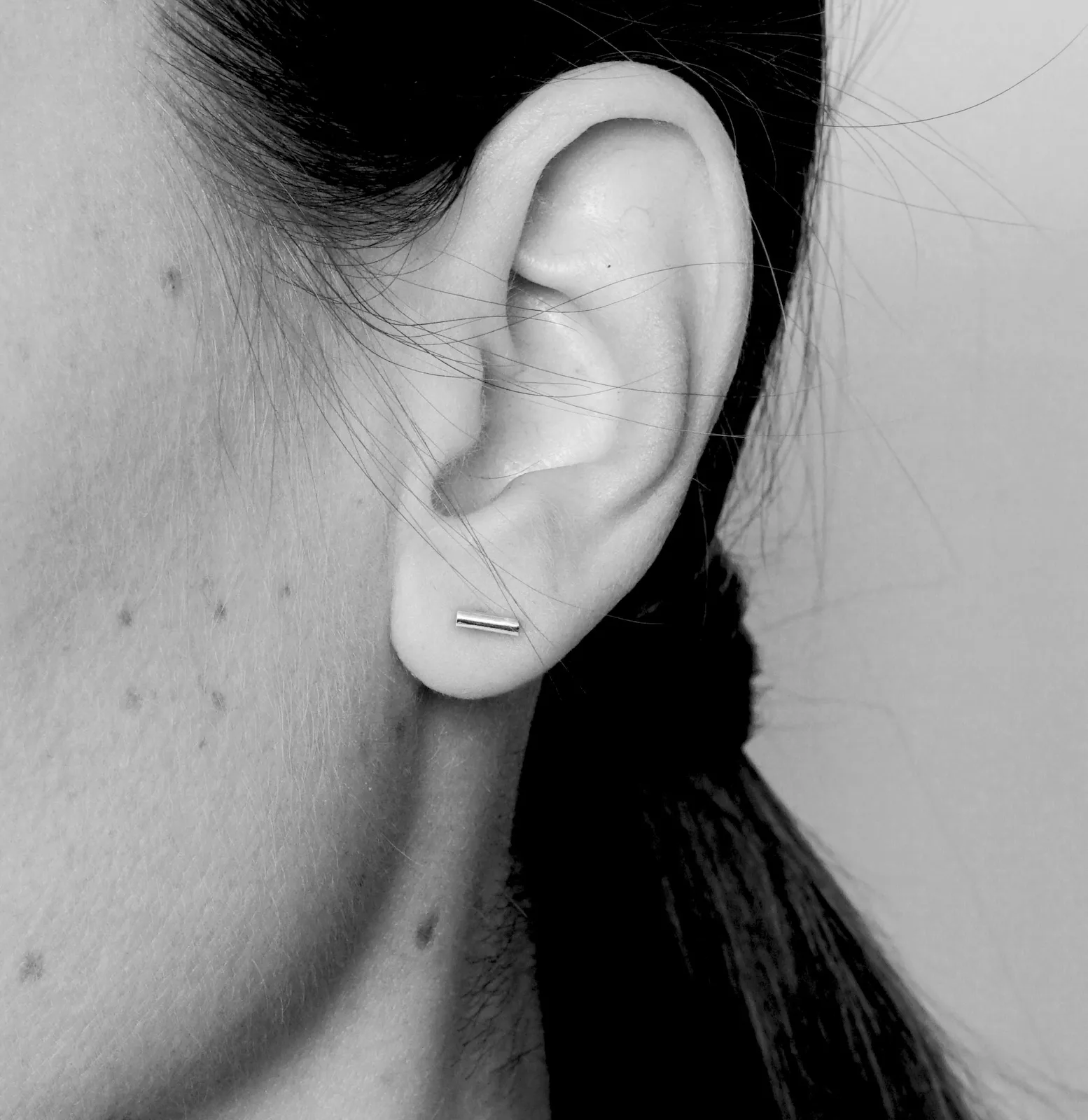 Close-up of a human ear wearing a tiny silver bar stud