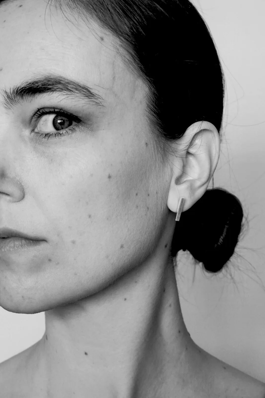 Close-up portrait of a woman in black and white wearing a small drop earring