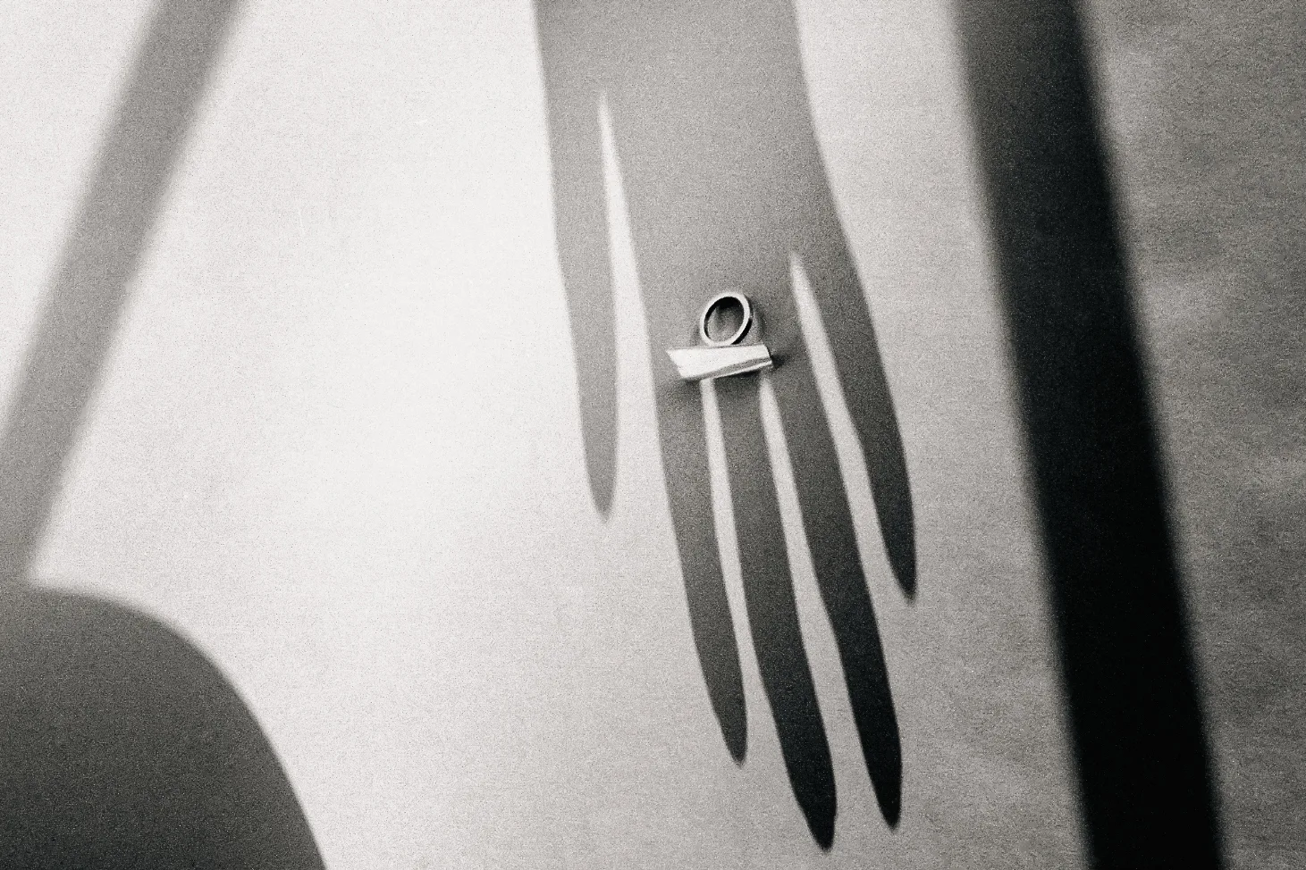 Shadow of a hand with long fingers cast on white, a geometric silver ring resting on top