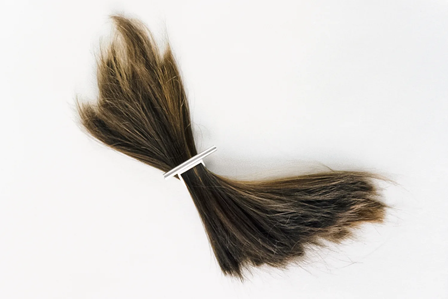 Silver bar ring wrapped around a tuft of brown human hair
