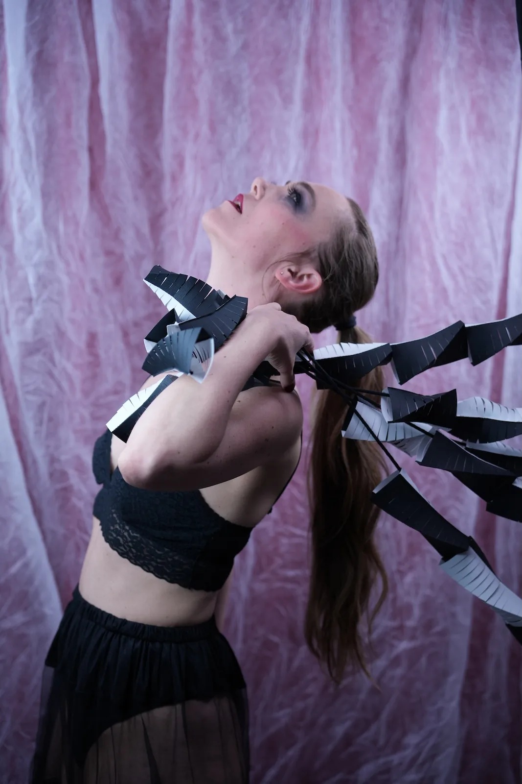 Model in a different pose wearing the same five-strand geometric black and white paper sculpture